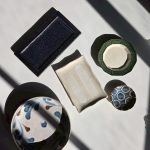 Group shot of the plates under hard sunlight: a black rectangular platter, a bamboo-rimmed green plate, a white hakeme plate and the indigo Yachimun mamezara